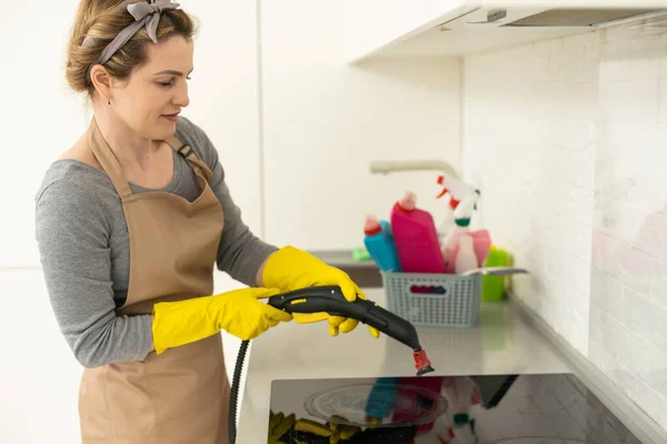 一个穿着制服的女人用蒸汽清洁剂清洗厨房炉罩的照片 而她的男同事则在后台工作 清洁服务的概念 家务劳动 — 图库照片