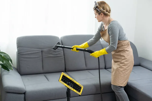 Woman cleaning couch with vacuum cleaner at home.