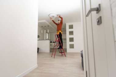 Üniformalı elektrikçi içeride tavan lambasını tamir ediyor..