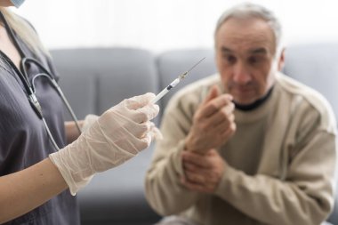 Doctor giving vaccination shot to elderly patient by syringe or injunction at home. concept of home health check to seniors during coronavirus covid-19 pandemic.