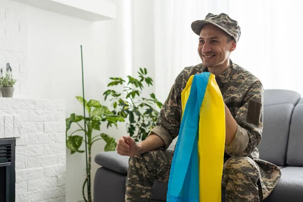 身穿军用象素制服的乌克兰战士手持乌克兰国家的黄蓝色旗帜 铁链上挂着一个三叉戟国家的小臂章 非常近 — 图库照片