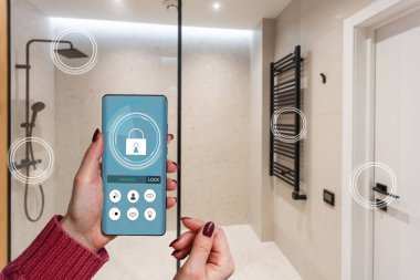 Akıllı ev telefonu, akıllı ev telefonu uygulama arayüzü cep telefonu ekranında, modern apartmandaki tüm ev sistemini telefonla kontrol eden genç bir kadın, konsept internet.