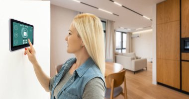 Akıllı ev sistemini kullanan ya da evden çıkmadan önce modern alarm sistemini çalıştıran hoş bir kadın. Mutlu kadın eve ya da daireye döndüğünde kolay güvenlik teknolojisini kapatıyor..