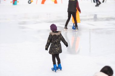Adorable little girl in winter clothes skating on ice rink.