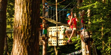 Erkek eğitmen, eğitim kampında iple giden yolda çocuğa yardım ediyor.