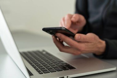 Bilgisayarla çalışan bir iş adamı, elinde akıllı bir telefonla. Bilgisayar masanın üstünde. İş konsepti