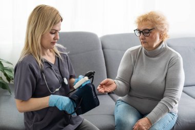 Bakıcı genç hemşire engelli ya da yaralı yaşlı kadının el ele tutuşmasına yardım ediyor. Sağlık sorunu olan yaşlı bir kadın engelli ve hastanede yürüyen bir kadın ile evde oturuyor.