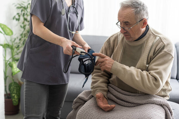 Молодая женщина врач в белой форме со стетоскопом проверки зрелого пациента кровяное давление на встрече в больнице, серьезный врач GP с помощью цифрового тонометра