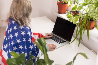 Positive teacher in headset having online lesson on laptop near flags in school.