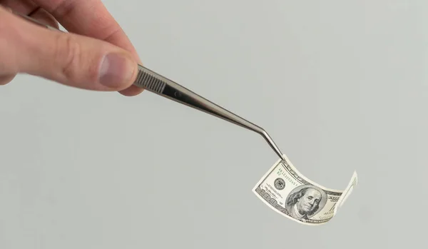 Lab, forensic scientist or medical professional with tweezers takes out rolled-up money. Hands in white gloves hold a test tube with a hundred dollar bill