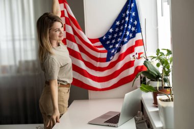 Amerikan bayrağıyla dizüstü bilgisayar kullanan mutlu genç bir bayan resmi. Kameraya bak. Yüksek kalite fotoğraf