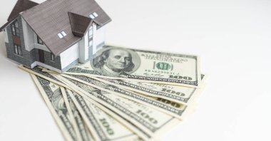 Küçük bir ev yüz dolarlık banknotlardan oluşan bir yelpazenin üzerinde yatıyor. Satın alınan evin anahtarları. Beyaz arka planda evin küçültülmüş kopyası. Yüksek kalite fotoğraf