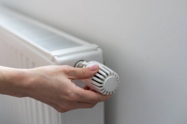 Bir kadın eli ısıtma termostatının sapını tutar. Isıtma hizmeti maliyeti konsepti, kamu maliyeti zammı. Yüksek kalite fotoğraf