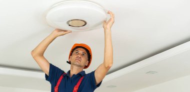 Bir elektrikçi tavana bir avize yerleştirir. Lambayı tavana kuran ve bağlayan bir elektrikçinin elleri