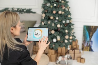 Woman controlling smart home devices using a digital tablet with launched application in the white room. Smart home concept.