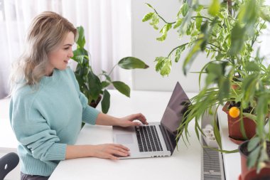 Mutlu gülümseyen, mavi gömlekli, mutlu bir çalışan iş kadını. Açık modern ofisteki bilgisayarlı, iş yerindeki beyaz masa başı işinde çalışıyor. Başarı kariyer konsepti