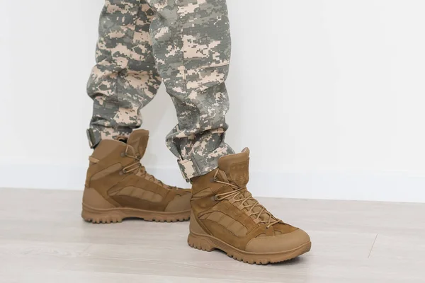 Legs of a soldier in camouflage and army boots on a gray background. Military conflicts and crises. Close-up.
