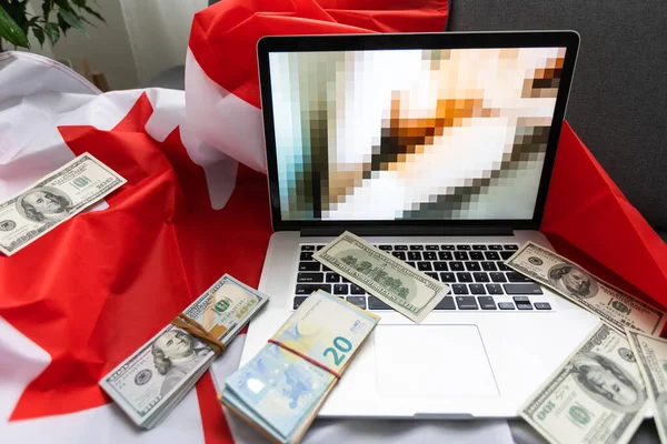 laptop with blurred screen, money and Canadian flag.