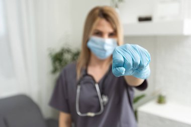 Tıbbi eldivenli bir doktor yakın plan bir yumruk gösteriyor. Koronavirüs salgını ve karantinanın kaldırılması durumunda kendini izole etme kavramı evde kalır.