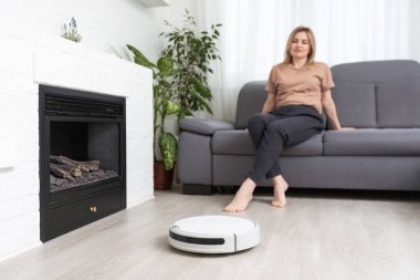 Kadın kanepede dinlenirken robot süpürgesi odayı temizliyor..