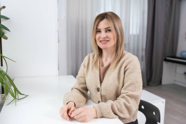 Güzel, neşeli bir kadın, sarışın, sıradan giyinmiş, kameraya tatmin edici bir şekilde bakıyor, mutlu. Güzel bir kadının stüdyo resmi. Boş bir stüdyo duvarında izole edilmiş..