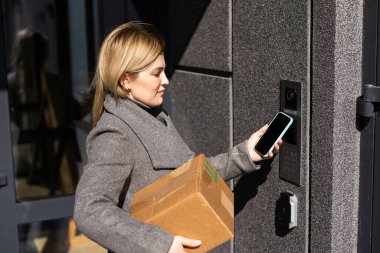 Dalgın sarışın kadın akıllı telefon kullanarak kapıyı açıyor. Ekran uygulamasını taklit ediyor. Kadın güvenlik sistemini cep telefonu kontrol kodu ile açıyor..