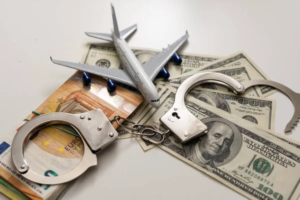 Handcuffs, toy airplane on money background.