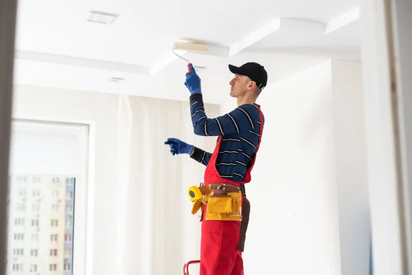 stock image man plasterer construction worker at work, takes plaster from bucket and puts it on trowel to plastering the wall, wears helmet inside the building site of a house