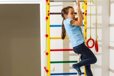 The girl smiles, plays and goes in for sports on the stairs and the Swedish wall in the childrens center in special tight clothes and leads a healthy lifestyle under the supervision of her parents.