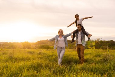 Mutlu aile: anne baba ve kız gün batımında doğada.