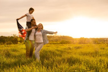 Buğday tarlasında mutlu bir aile ve arkasında Amerikan bayrağı var.