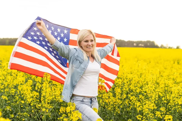 Kolza Tohumu Tarlasında Rüzgarda Amerikan Bayrağı Tutan Çekici Bir Kadın — Stok fotoğraf