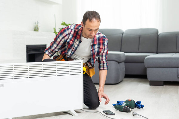 Workman mounting water heating radiator near the window in the white renovated living room, Image with copy space. High quality photo