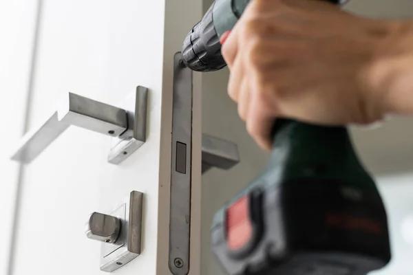 A locksmith is repairing an interior door lock. Close-up of male hands repairing or replacing an entrance door lock with a hex screwdriver. High quality photo
