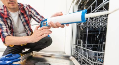 Bulaşık makinesinin kurulumu. Genç Afrikalı servis elemanı yeni şık mutfağa bulaşık makinesi kuruyor. İş kıyafetlerindeki Diverce tamircisi, yakın portre. Yüksek kalite fotoğraf