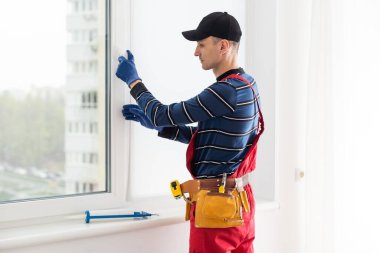 Mavi gömlekli adam pencere kurulumu yapıyor..