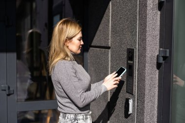 Kadın, cep telefonundaki uygulamayı kullanarak erişimi sağlamak ve binadan geçmek için gizli anahtar kodu giriyor, akıllı ev sistemini etkisiz hale getirmek için kontrol panelindeki düğmelere basıyor.