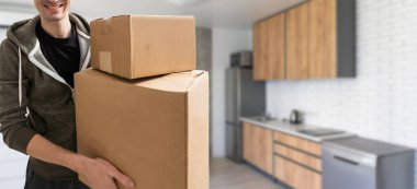 Karton kutu taşıyan hevesli genç adam, evden taşınıyor..