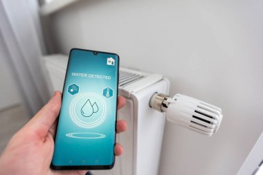 Akıllı ev uygulaması olan telefonu elinde tutan bulaşık makinesini uzaktan kontrol eden bir adam. Akıllı mutfak aletleri konsepti. Yüksek kalite fotoğraf