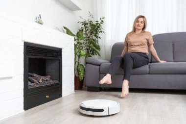 Kadın kanepede dinlenirken robot süpürgesi odayı temizliyor..