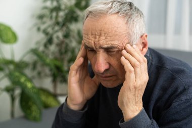 Oturma odasında migrenden muzdarip yaşlı bir adam baş ağrısı çekerken ve kafasına dokunurken olgun bir adam el ele verip dayanılmaz bir acıdan muzdarip olur.