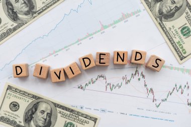 Hisse senedi grafiği ve dolar arkaplanlı harf küpü üzerindeki temettü kelimesinin kavramsal görüntüsü. Yüksek kalite fotoğraf