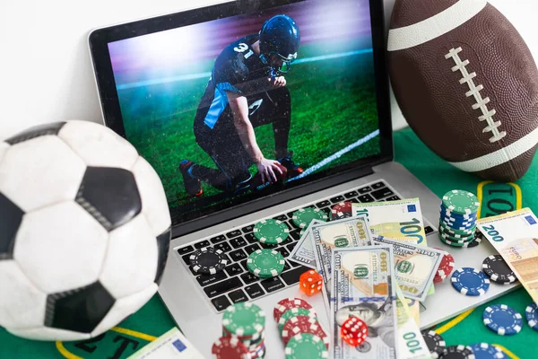 Ноутбук із зображенням гравця в американський футбол на екрані, грошей, фішками для покеру, спортивними м'ячами