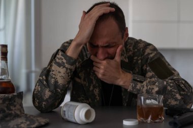 Kamuflajlı bir adam ordudan döndükten sonra depresyona girer. Alkol ve uyuşturucu hapları kullanıyor. Ağır anılar yüzünden acı çekiyor. Masanın üzerinde bir silah var. Yüksek kalite fotoğraf