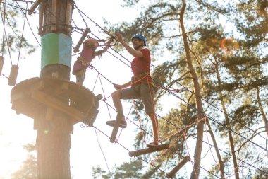 Erkek eğitmen, eğitim kampında iple giden yolda çocuğa yardım ediyor.