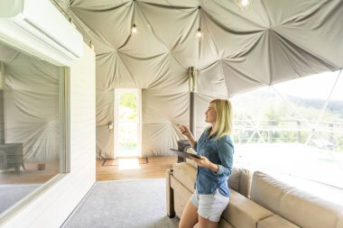 woman holding a tablet computer with system clever house on a screen on the background of the house.