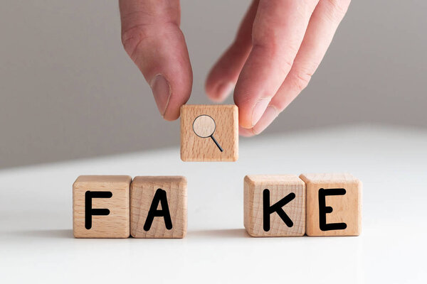 Слово "FAKE" пишется деревянными буквенными плитками на белом фоне. Высокое качество фото
