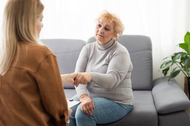 Destekçilerin yakın çekimi. Genç bir kadının, yaşlı bir kadının elini rahatça tutarken yakın plan fotoğrafı. Yaşlı bir kadının elini tutan kadın bakıcı..