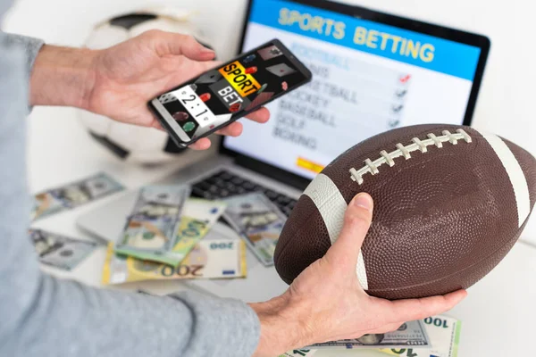 Man betting on sports using smartphone and laptop at table, closeup. Bookmaker websites on displays. High quality photo