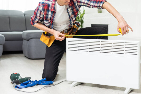 Workman mounting water heating radiator near the window in the white renovated living room, Image with copy space. High quality photo